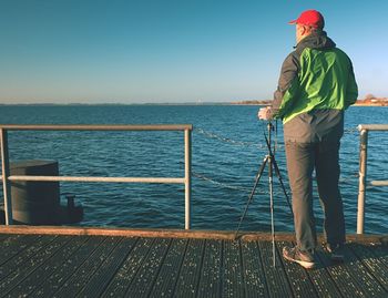 Alone tourist takes photos with camera and tripod on wooden pier board. hot sun, , smooth sea