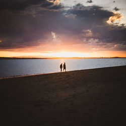 Silhouette people on beach against sky during sunset