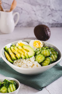 Bowl with cottage cheese, cucumber and avocado slices and boiled egg on the table vertical view