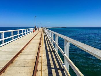 Pier on sea against clear blue sky