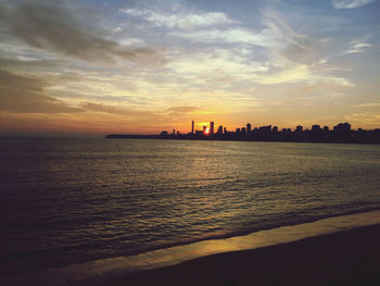 Silhouette city by sea against sky during sunset