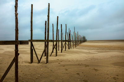 Wooden posts on beach against sky