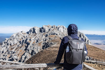 Rear view of man on rock against blue sky