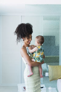 Happy woman carrying baby boy in bedroom at home
