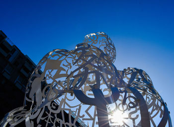 Low angle view of sculpture against building against clear blue sky