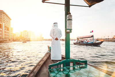 Rear view of man standing in boat on river at sunset