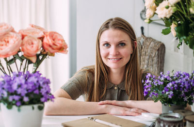 Portrait of young woman with flowers in vase on table