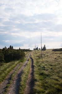 Dirt road amidst field against sky