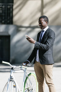 Side view of businessman using phone while standing on road with bicycle