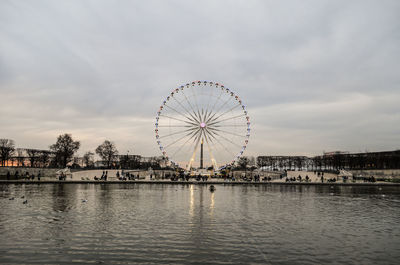 Ferris wheel by river against sky