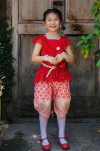 Portrait of smiling girl standing against red wall