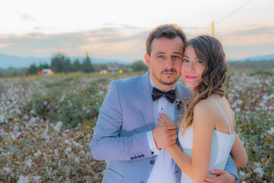 Portrait of smiling bride and groom standing on field