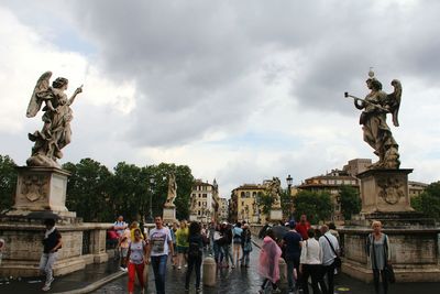 Statue of people in city against cloudy sky