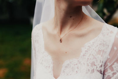 Gold pendant around neck of bride in a white dress with veil. blurred background
