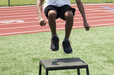 Front view of a young athlete jumping onto a plyo box during a high school summer sports camp.