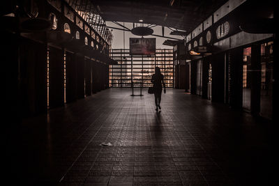 Rear view of man walking on illuminated footpath in building