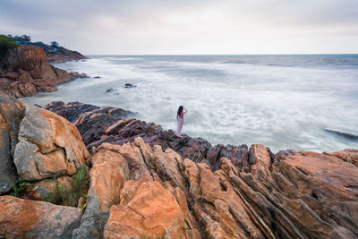 High angle view of woman standing on rock formation by sea