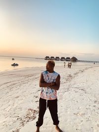 Rear view of woman standing at beach against clear sky during sunset