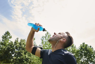 Young man drinking drink in bottle against sky