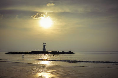 Lighthouse by sea against sky during sunset