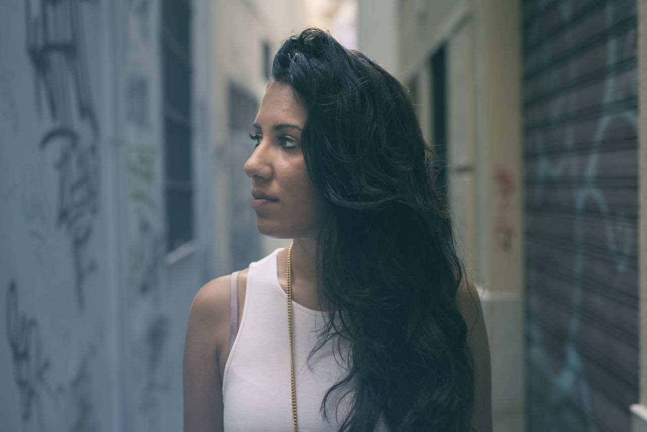 young adult, young women, headshot, lifestyles, looking away, focus on foreground, contemplation, long hair, casual clothing, beauty, person, black hair, thoughtful, city life