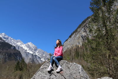 Full length of woman sitting on rock amidst mountain range against blue sky