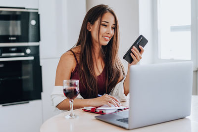 Young woman using phone while sitting on laptop