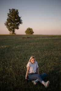 Woman sitting on field against sky during sunset