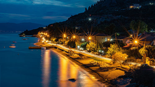 Illuminated city by street against sky at night