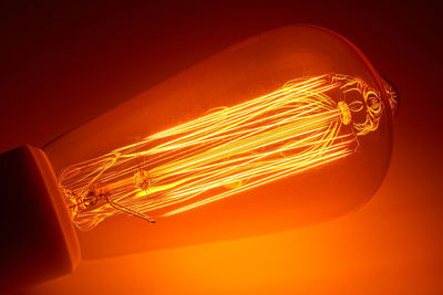 Close-up of illuminated light bulb against orange background