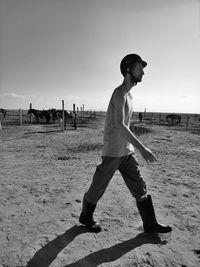 Side view of young man walking at farm with horses in background