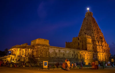 People at illuminated temple building against blue sky at night