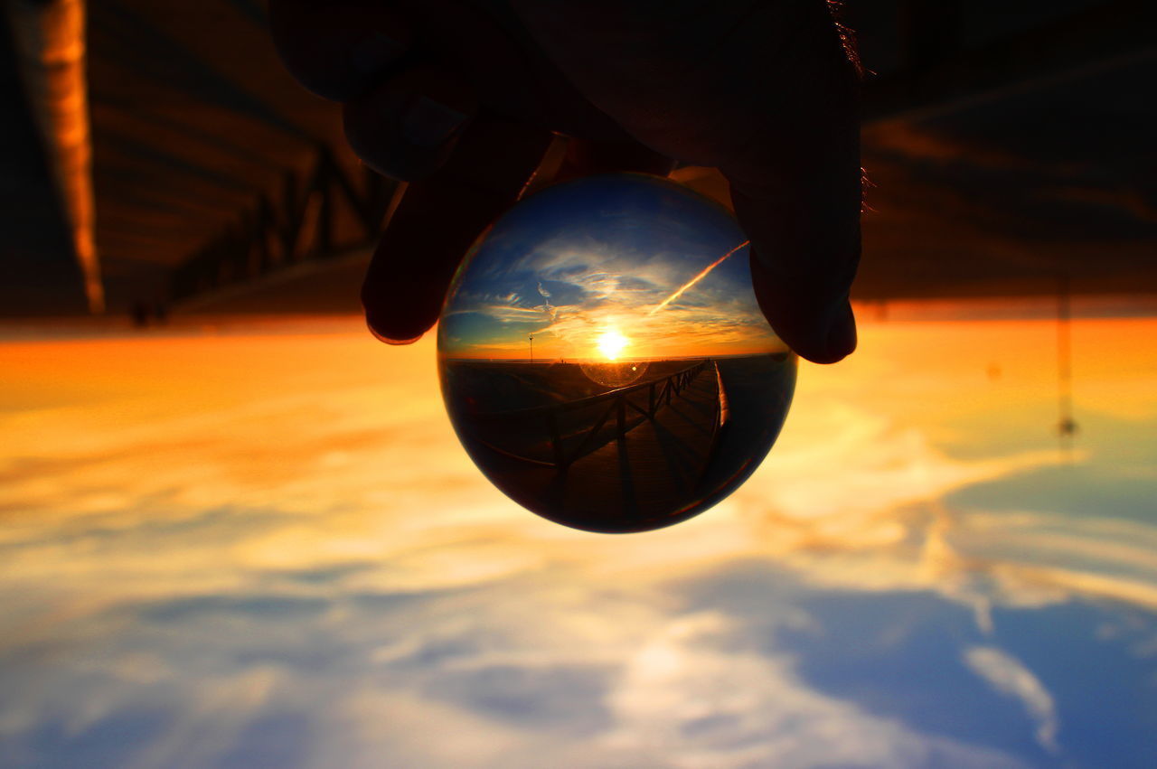 CLOSE-UP OF HAND HOLDING BALL AGAINST SUNSET SKY