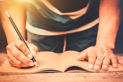 Midsection of man writing in book on table