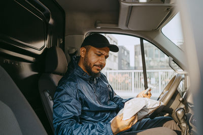 Confused male delivery person reading parcel details while sitting in van