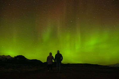 Rear view of people standing on land against sky at night