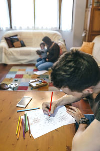 High angle view of father coloring on paper over table with pregnant mother and son playing in background