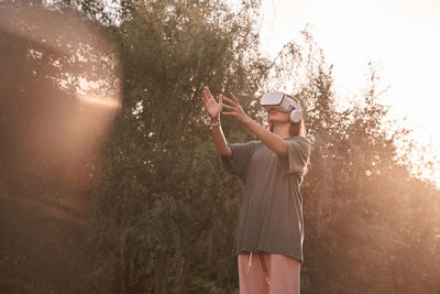 Front view of woman in vr helmet standing against trees