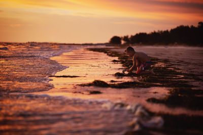 Boy playing at shore of beach during sunset