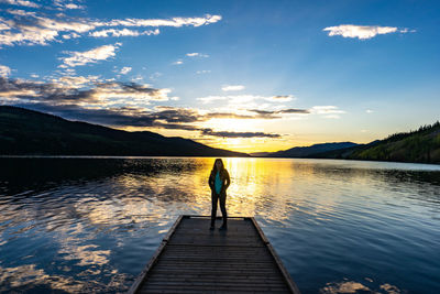 Man standing on pier over lake against sky during sunset