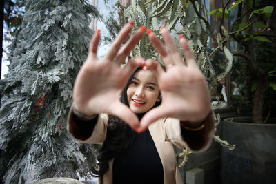 Portrait of smiling young woman gesturing against plants