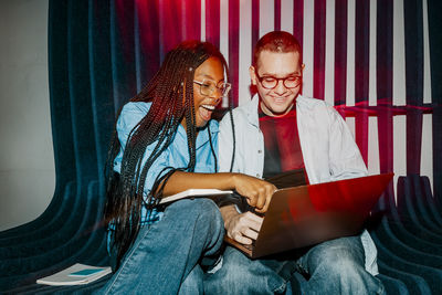 Female entrepreneur with mouth open pointing at laptop while sitting next to colleague at office