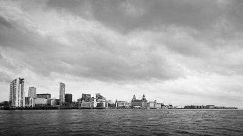 City at waterfront against cloudy sky