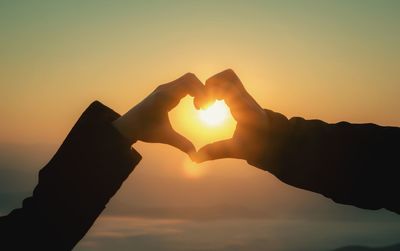 Close-up of hand holding heart shape against sunset sky