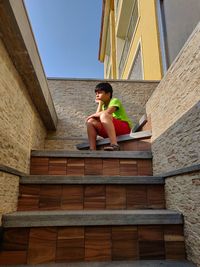 Low angle view of boy sitting on staircase against sky