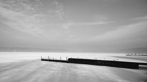 Pier on frozen lake against sky