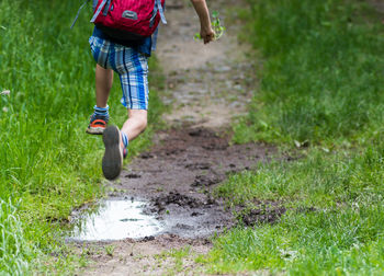 Low section of boy jumping over puddle on field