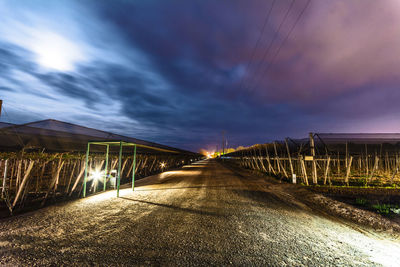 Road by illuminated bridge against sky at night