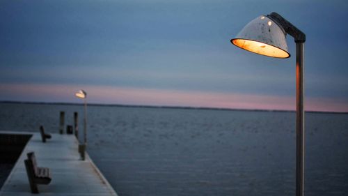 Street light by sea against sky at sunset