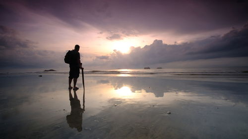 Silhouette man standing on beach against sky during sunset